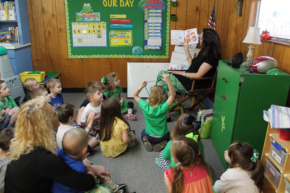 Adult reading a book to children sitting on the floor in a classroom