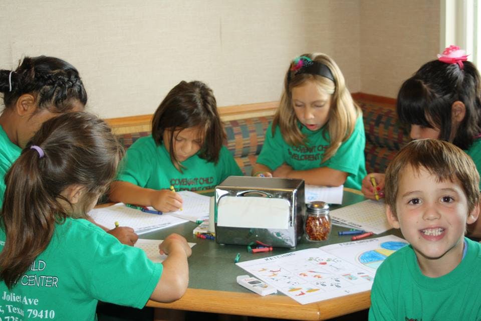 Children in green shirts writing at a table