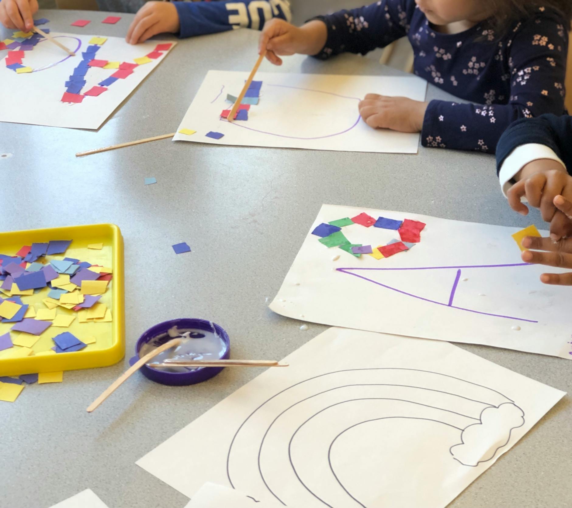 Children doing crafts with paper squares and glue