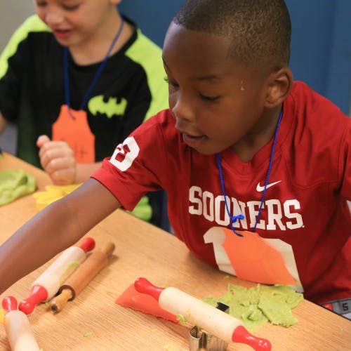Child in red shirt playing with dough and rolling pins