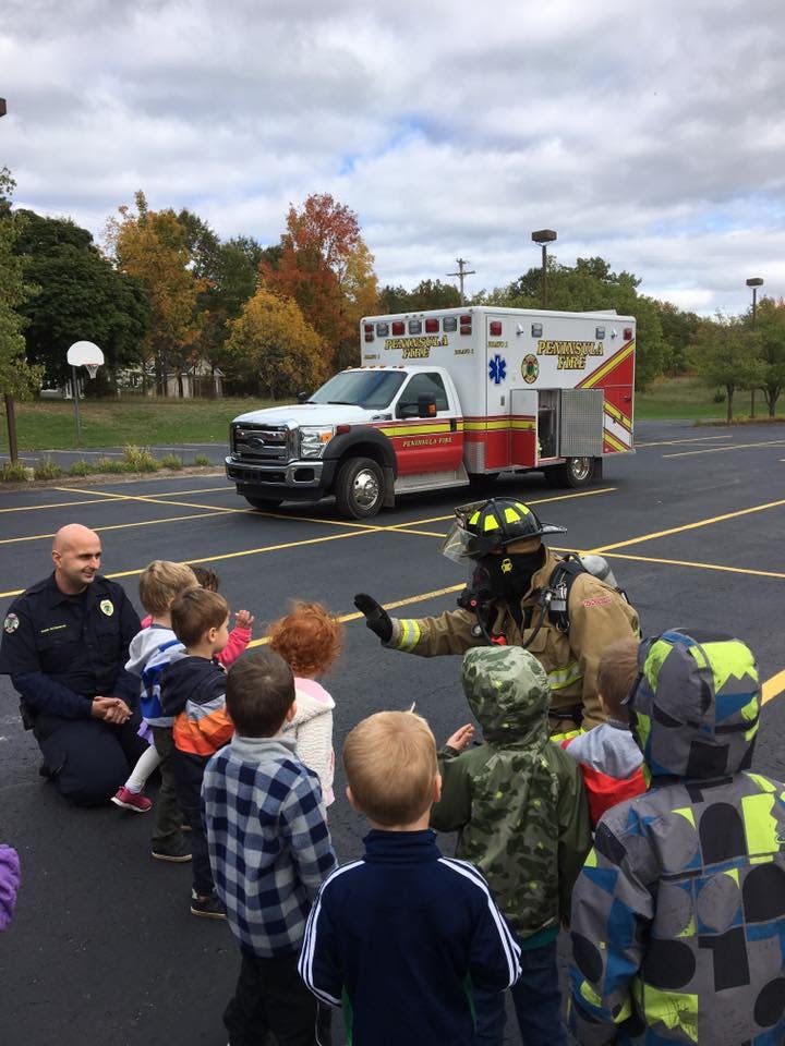 Firefighter in gear talking to children with an ambulance in the background