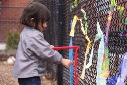 Child playing with colorful ribbons on a fence