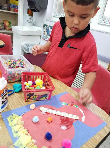 Child making a craft with pom-poms and glue