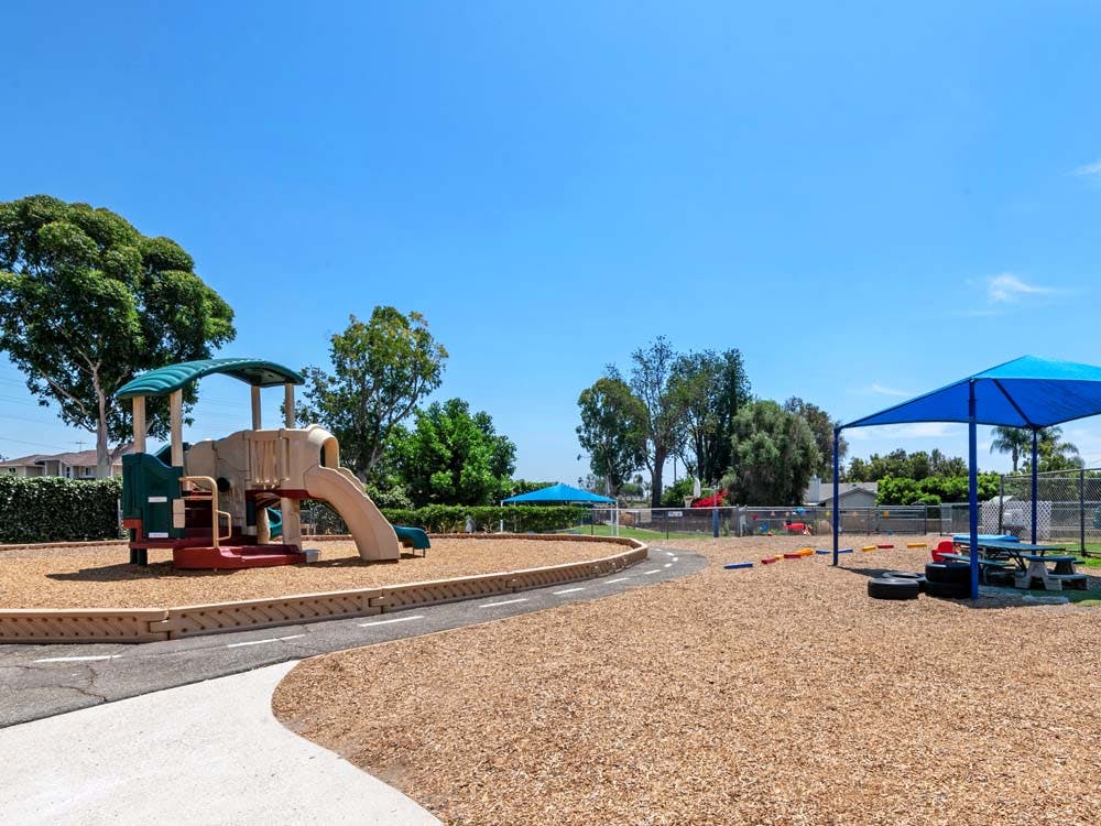 A children's playground with wood chips, slides, and a blue shade canopy