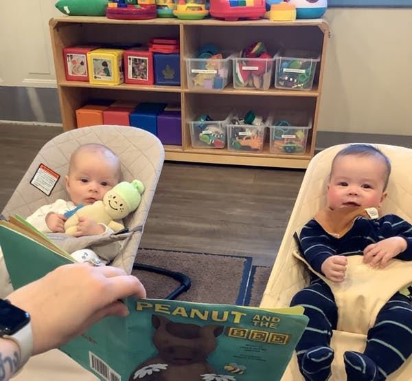 Two babies in bouncers with a person holding a book