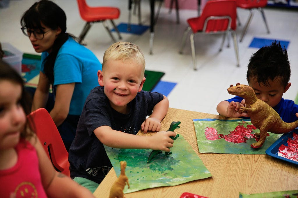 Child playing with dinosaur toys at a table in a classroom