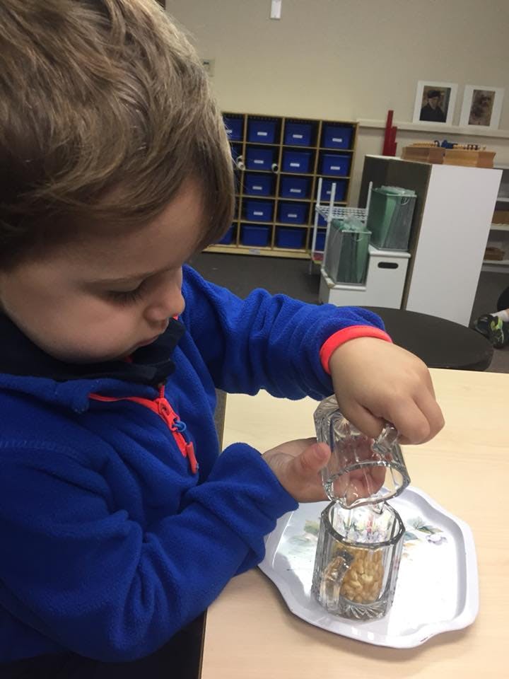 Child pouring from one glass to another in a classroom