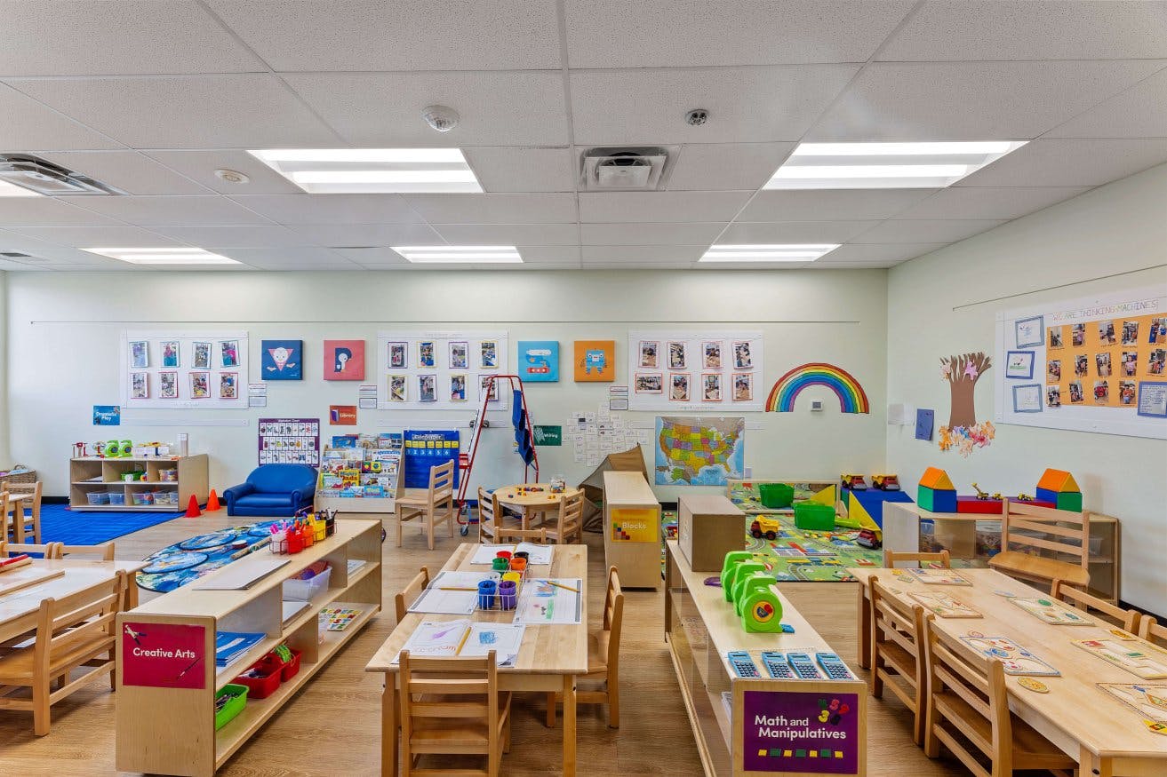 Empty classroom with small tables and chairs, various activity centers, and wall decorations