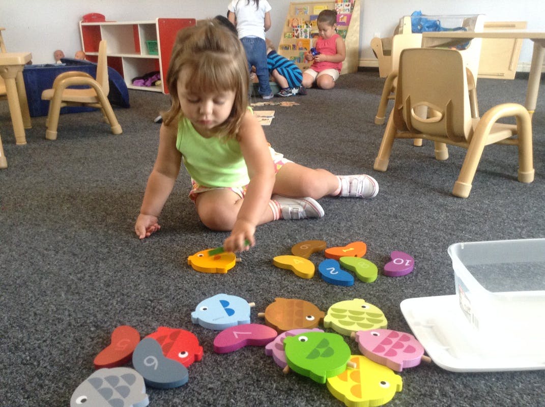 Child playing with colorful fish-shaped toys on the floor in a classroom