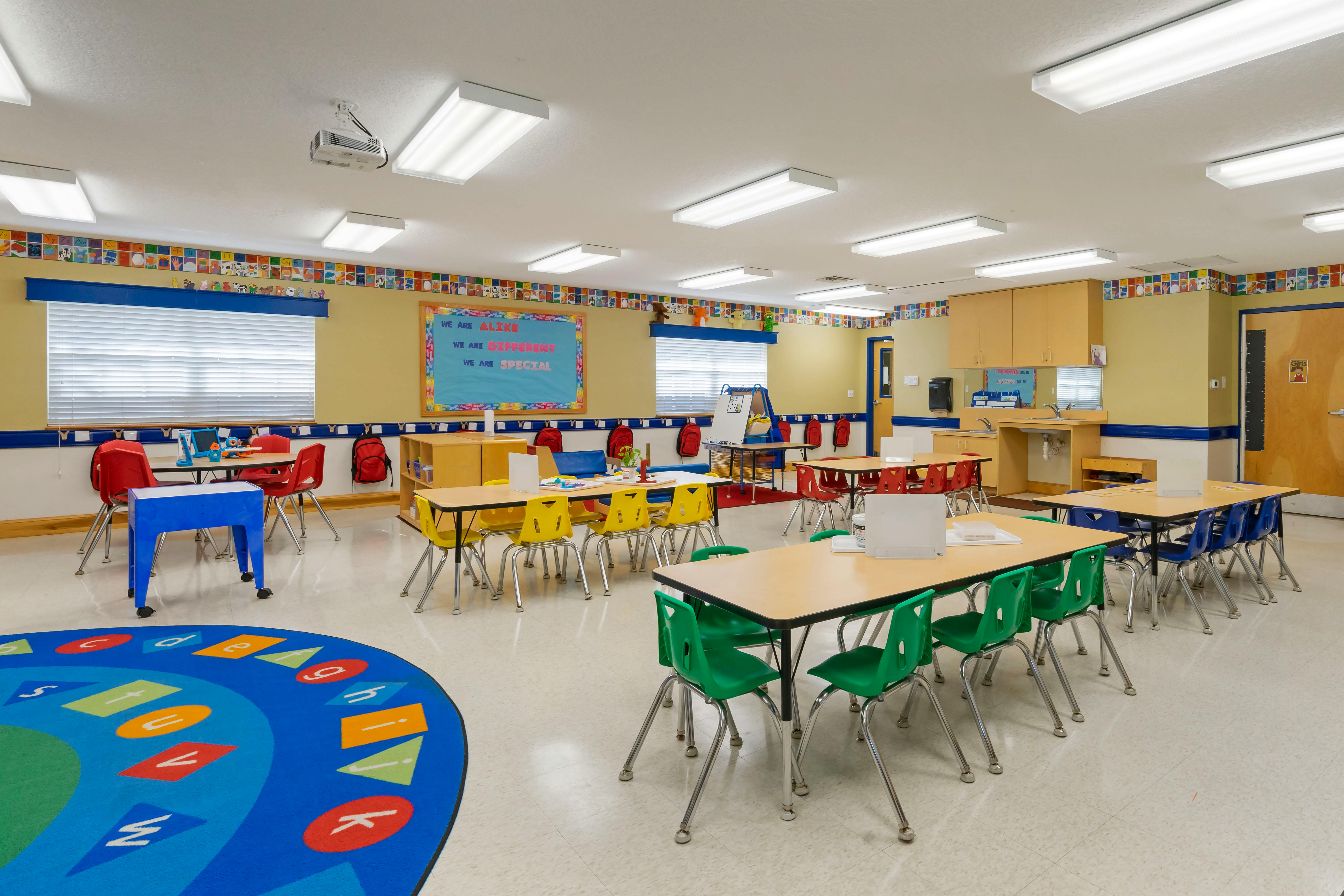 Empty classroom with small tables and chairs, and a colorful rug