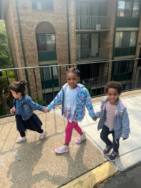 Three children holding hands and walking on a sidewalk