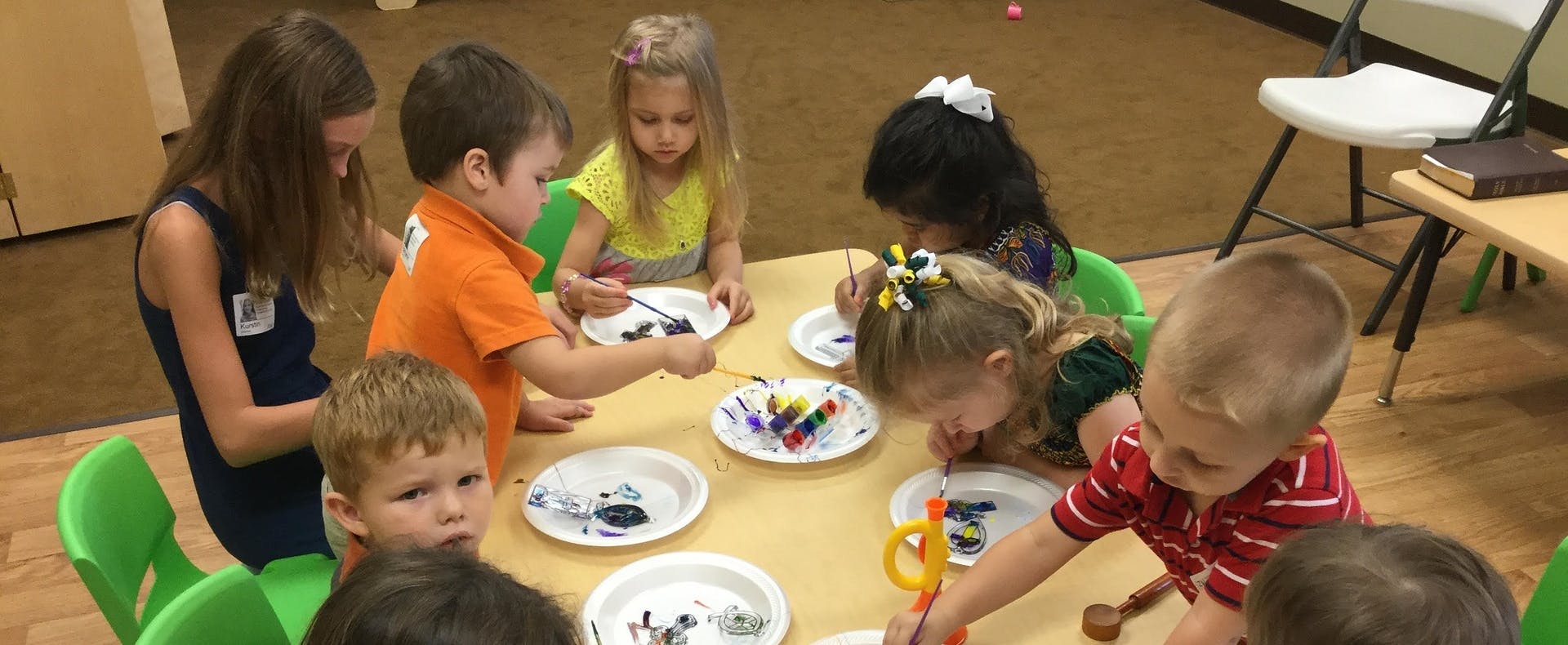 Children and a teen at a table with plates and art supplies