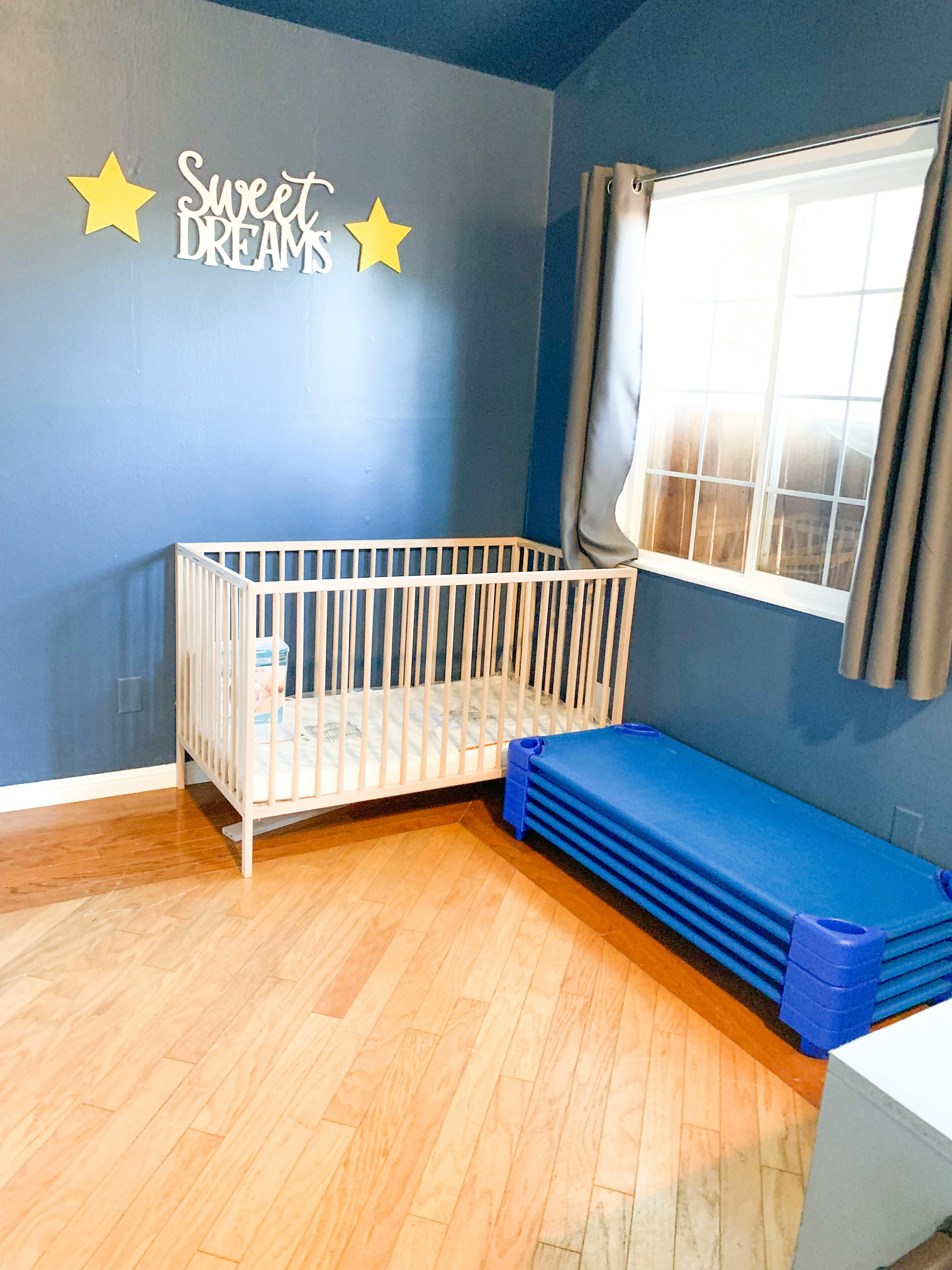 Crib and stacked blue cots in a room with blue walls and a window