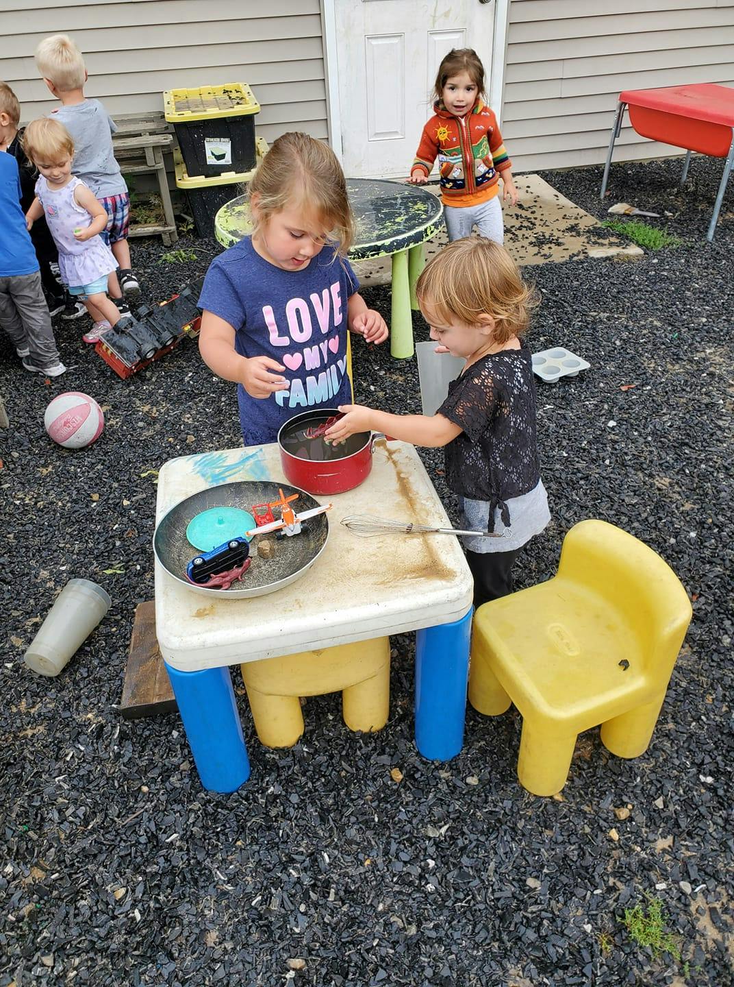 Two children playing with pots and pans at a small table outdoors