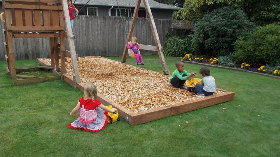 Children playing on a wooden swing set with wood chips