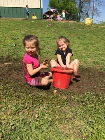 Two children playing in mud with a red bucket