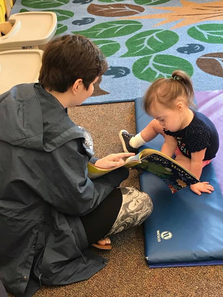 Person reading a book to a child sitting on a mat