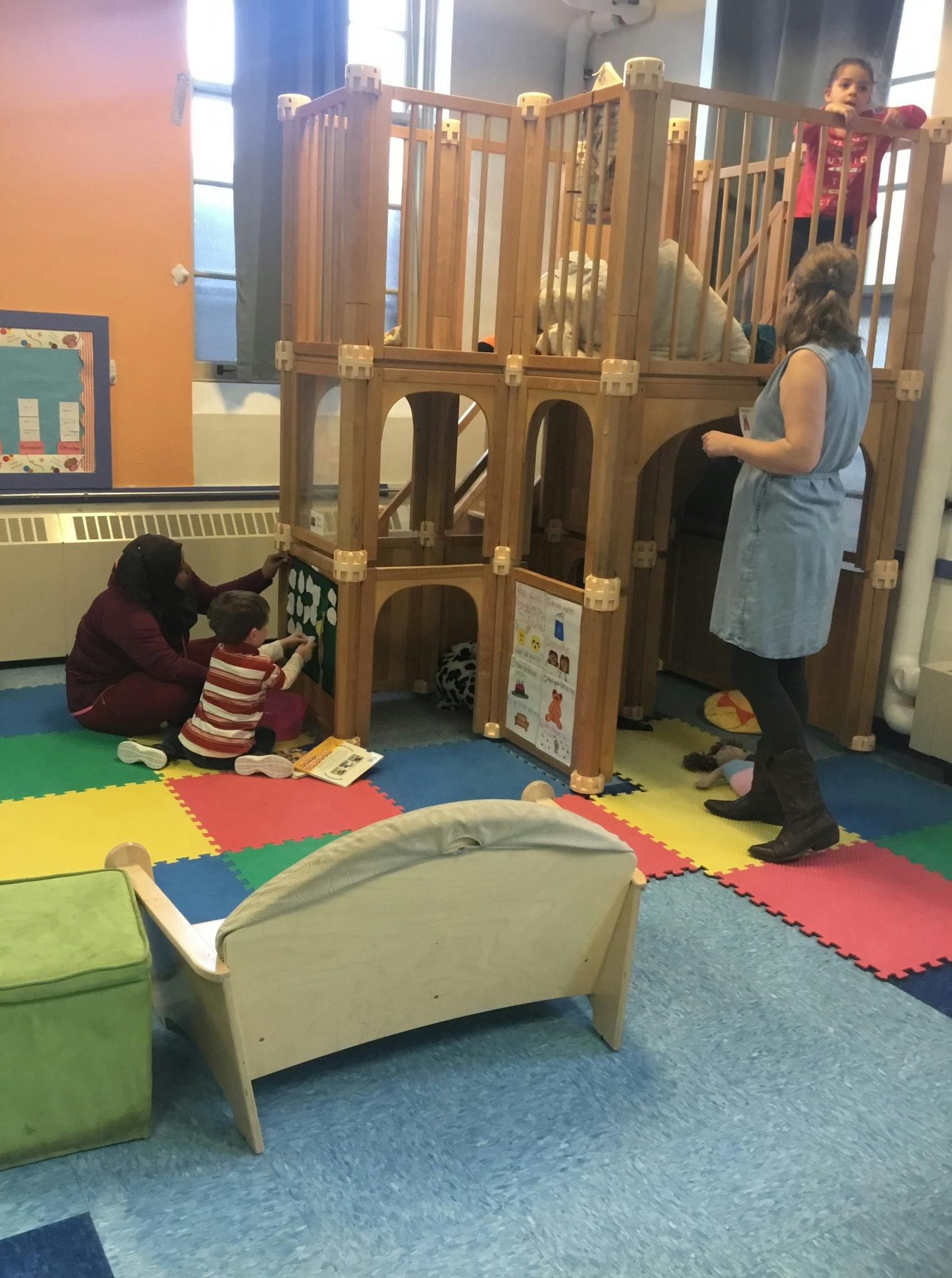 People and children playing on a wooden play structure in a room