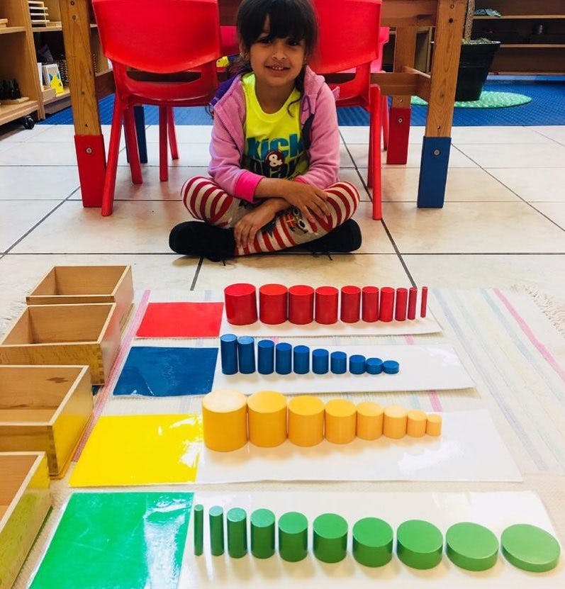 Child sitting on floor with colorful cylindrical blocks arranged in rows