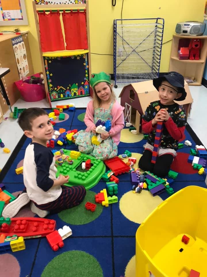 Three children playing with building blocks on a colorful rug