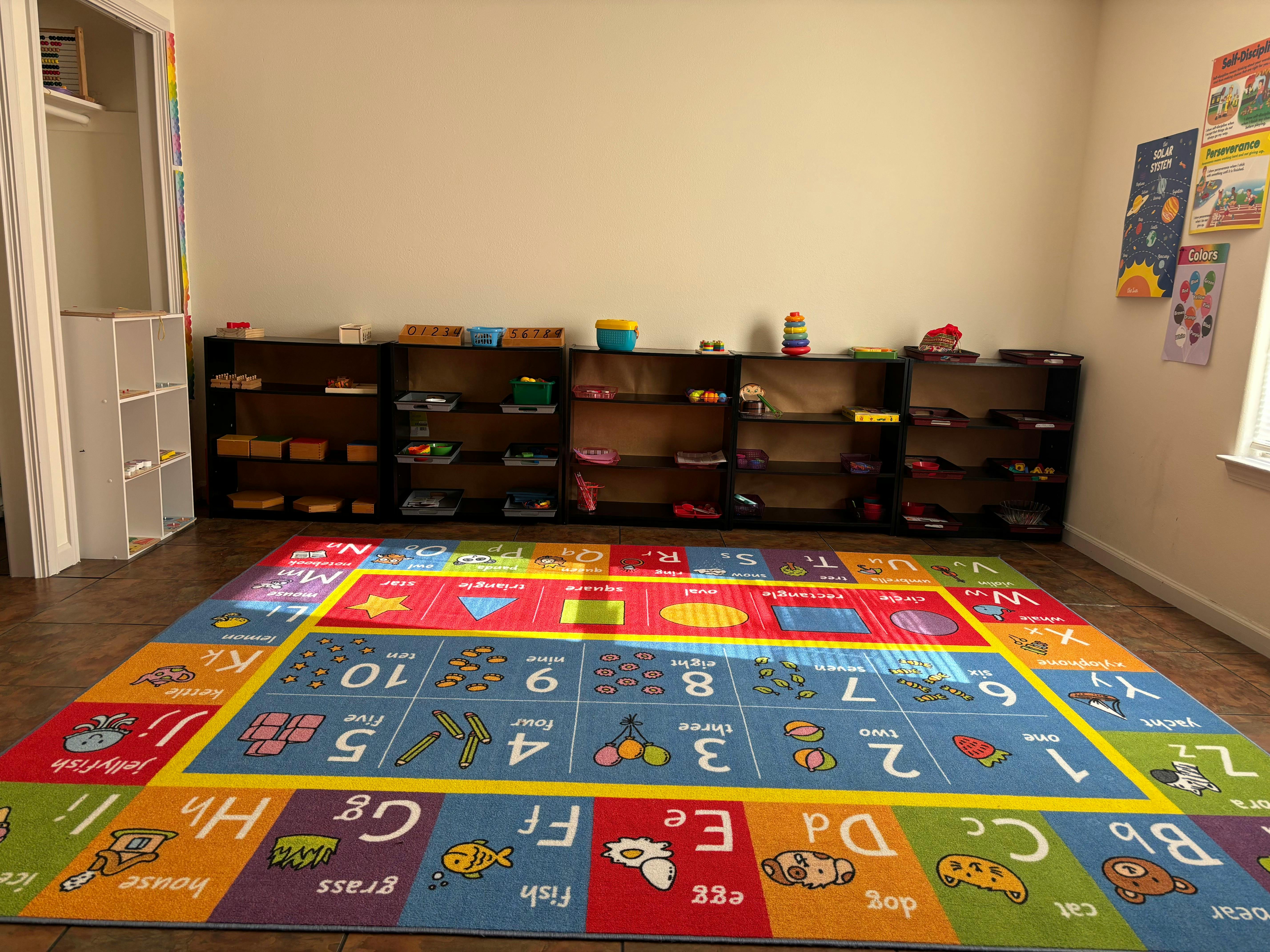 Colorful alphabet and number rug in a classroom with shelves of learning materials