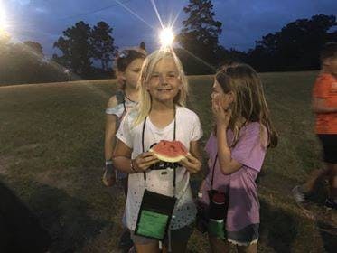Child holding a slice of watermelon at night
