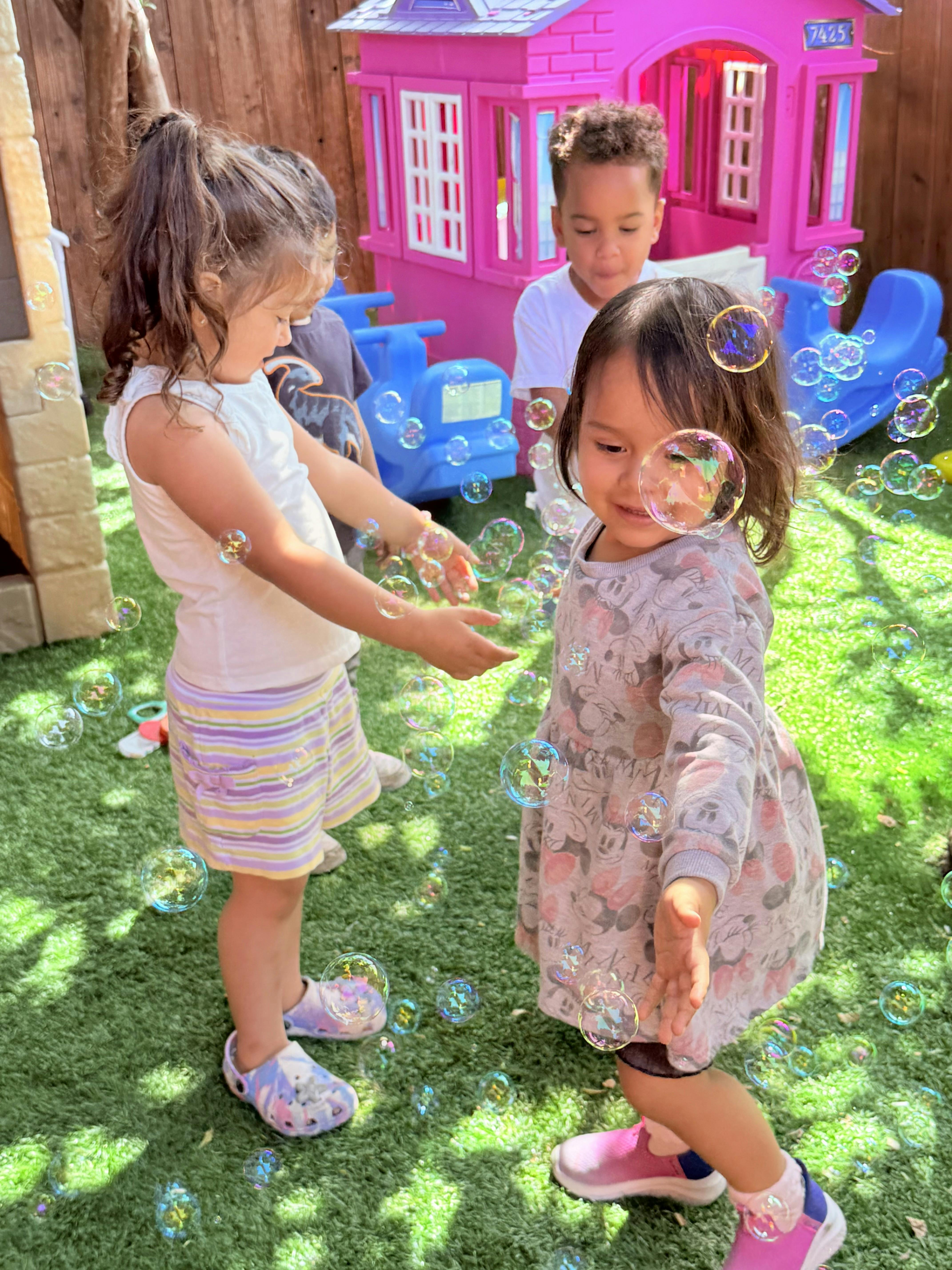 Two children playing with bubbles outdoors, another child in the background