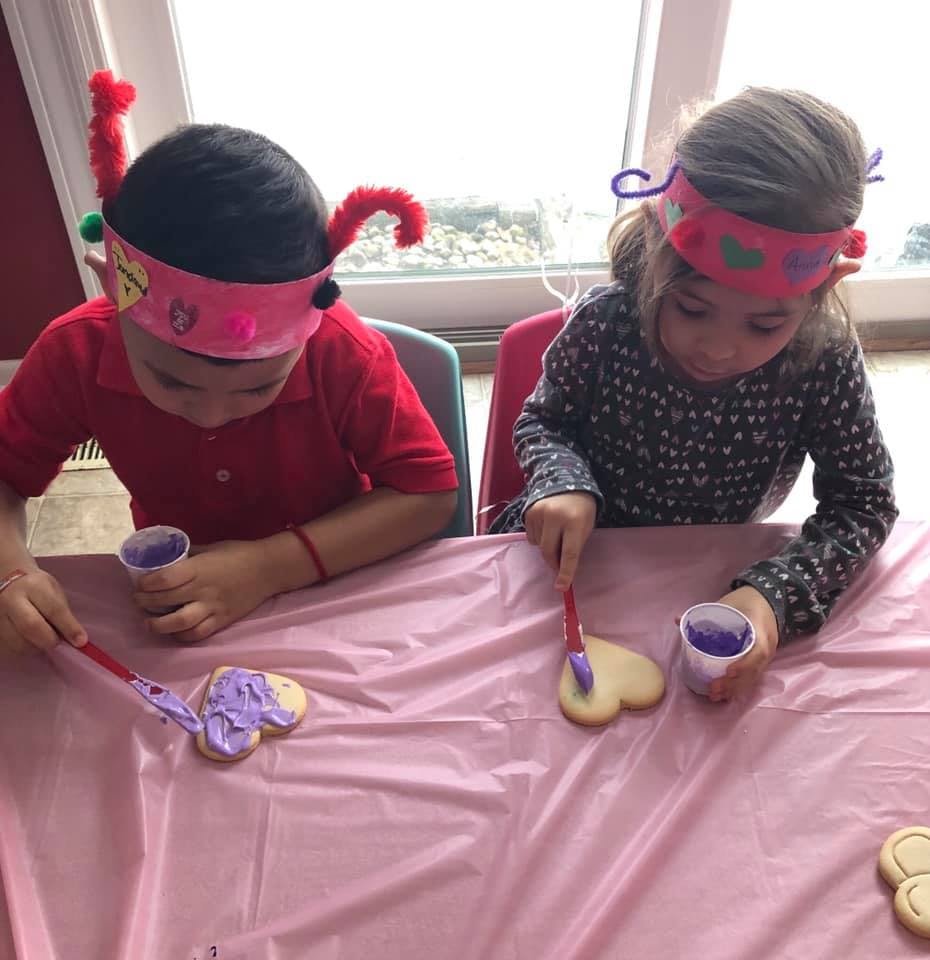 Two children decorating heart-shaped cookies with purple frosting