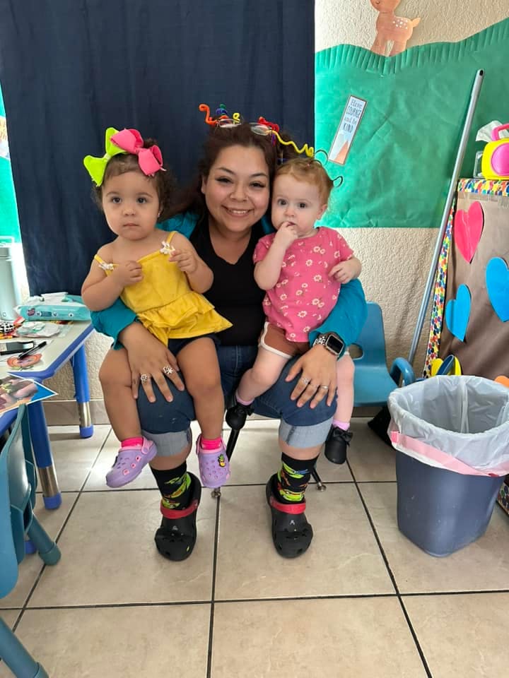 Person holding two children, one in yellow and one in pink
