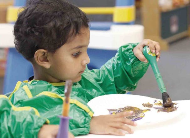 Child in smock painting with a brush
