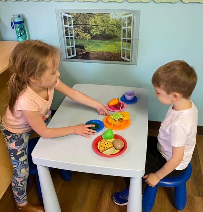 Child and teen playing with toy food at a small table