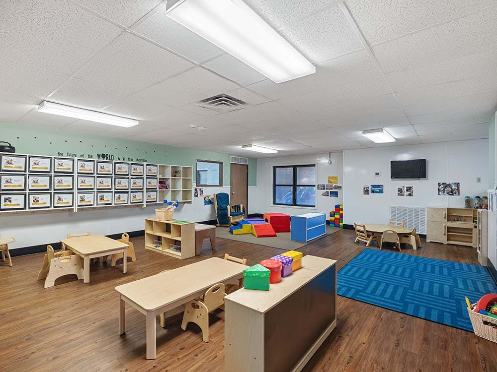 Empty classroom with small tables and chairs, play mats, and toys