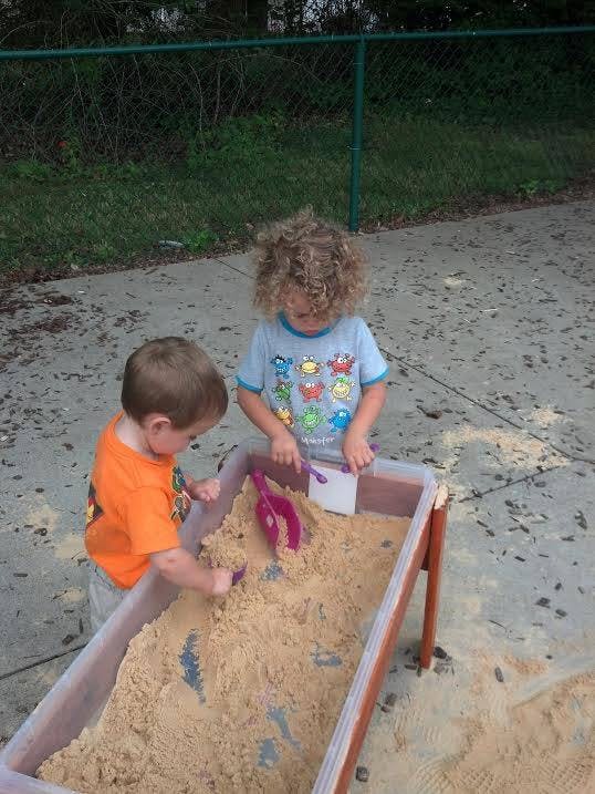 Two children playing in a sandbox with shovels