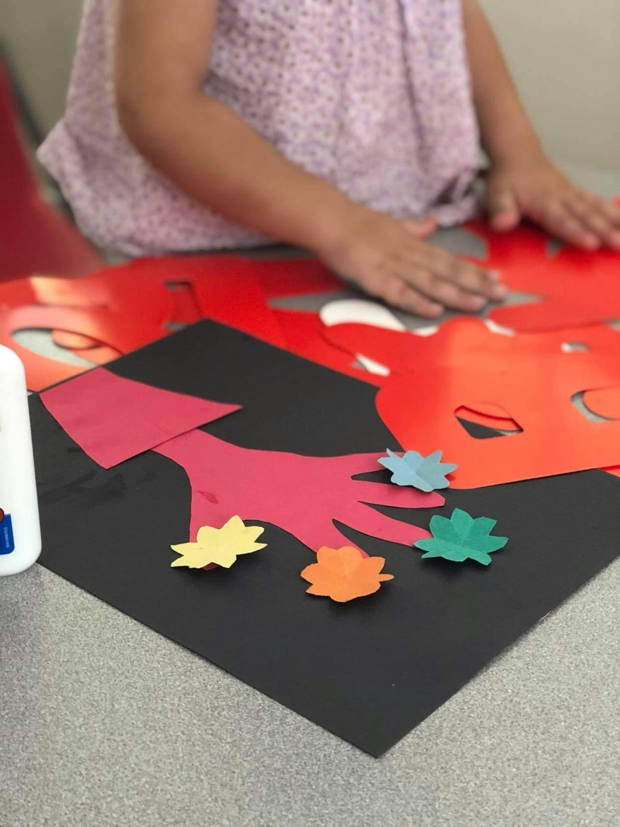 Child making a paper craft with cutouts and glued paper shapes