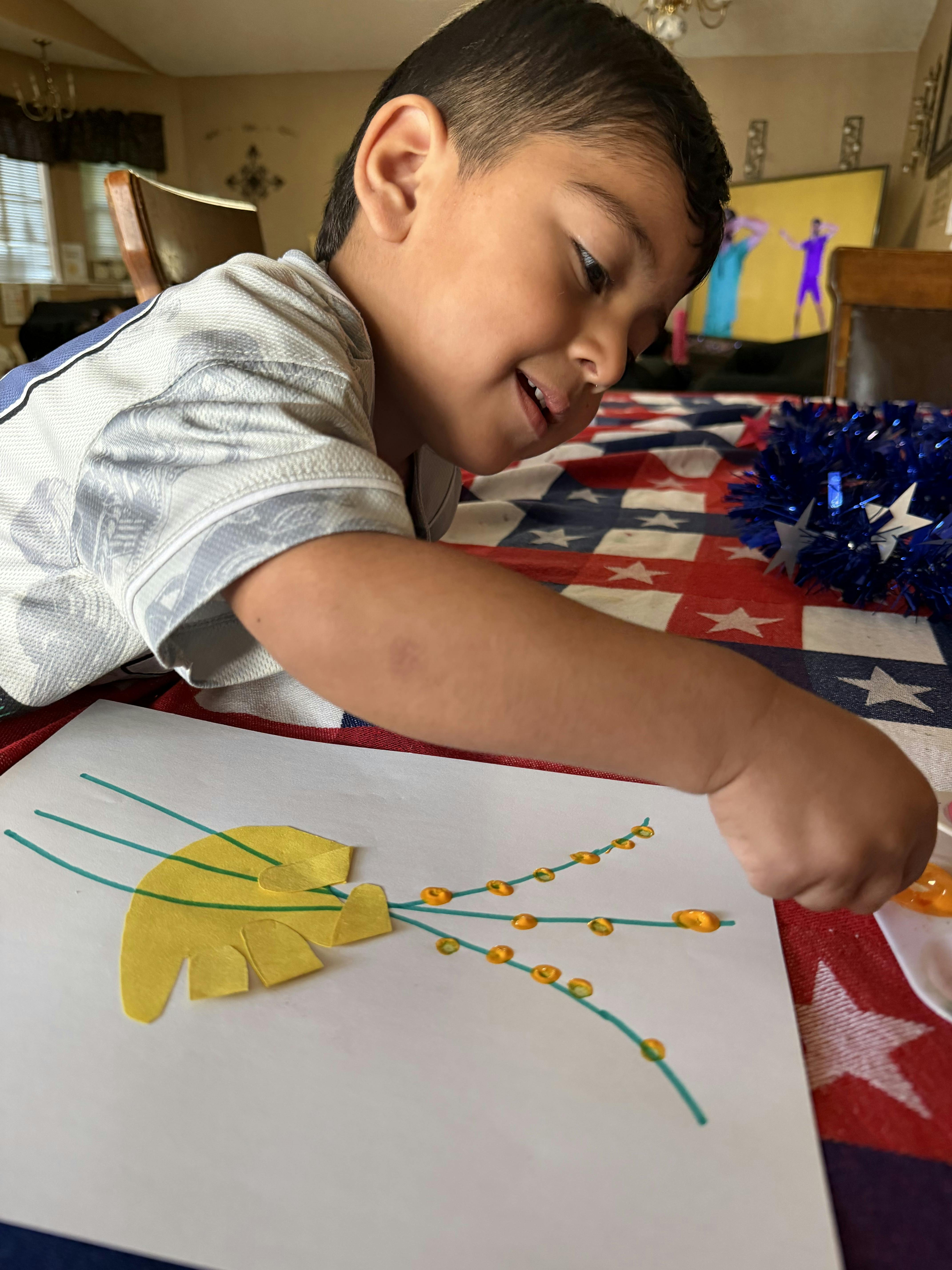 Child smiling while doing a craft on a red, white, and blue tablecloth