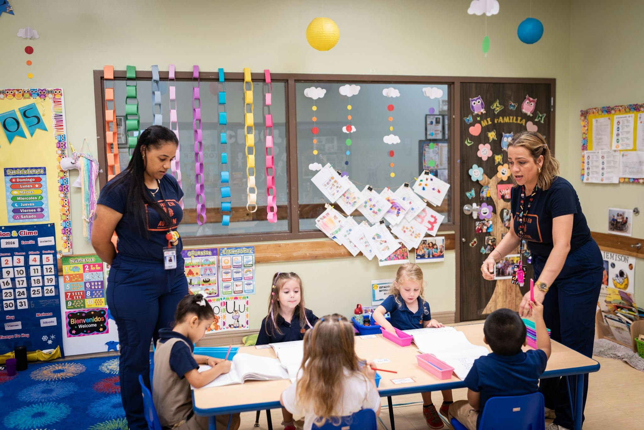 Two people supervising children at a table in a classroom