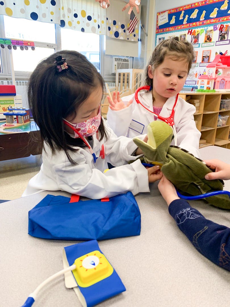 Two children in lab coats playing with a stuffed animal and medical toys
