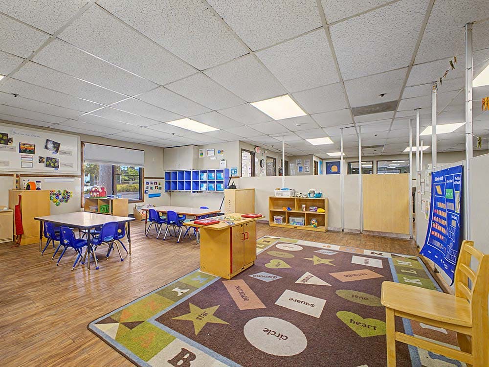 Classroom with tables, chairs, shelving, and a patterned rug