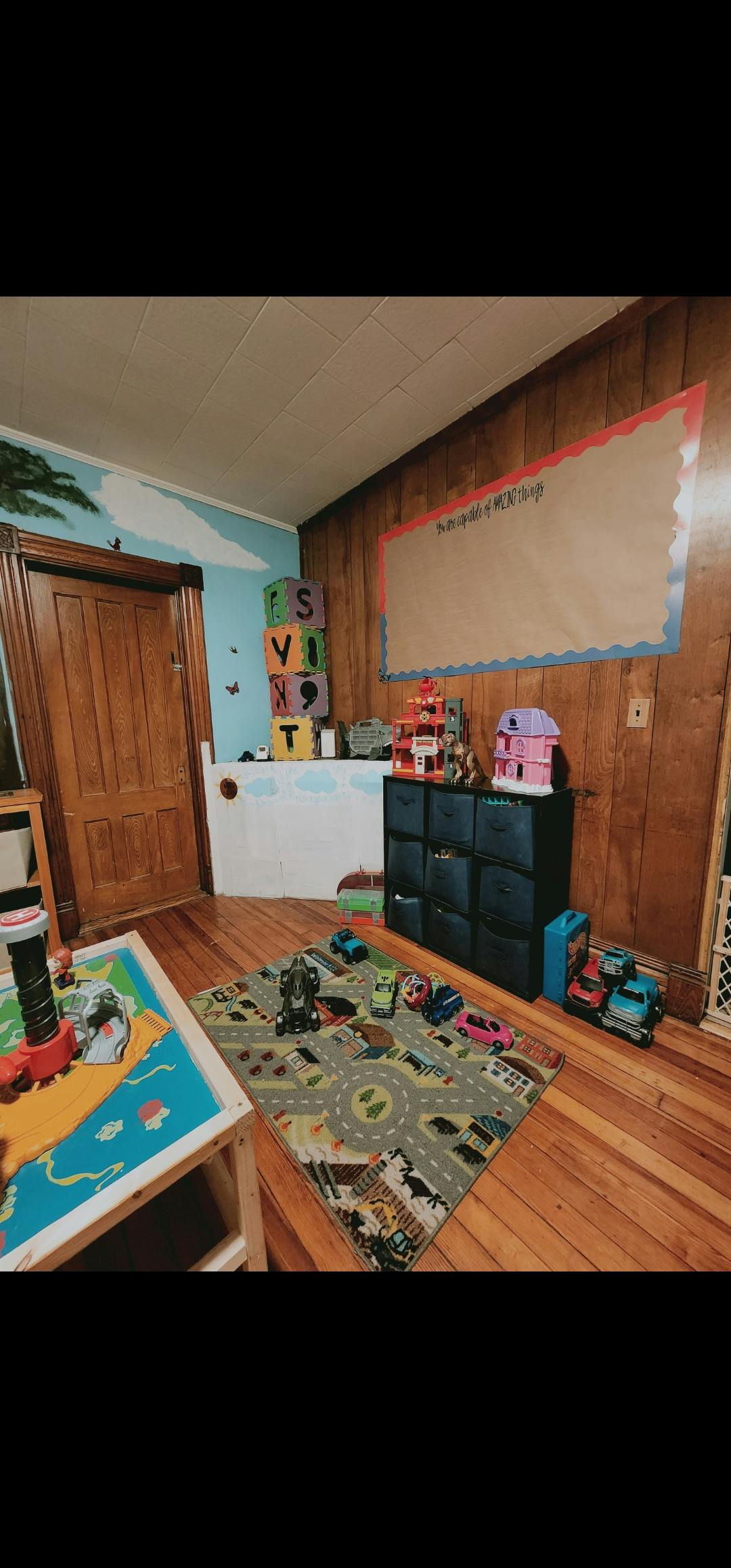 Playroom with a road map rug, toys, and a large blank bulletin board