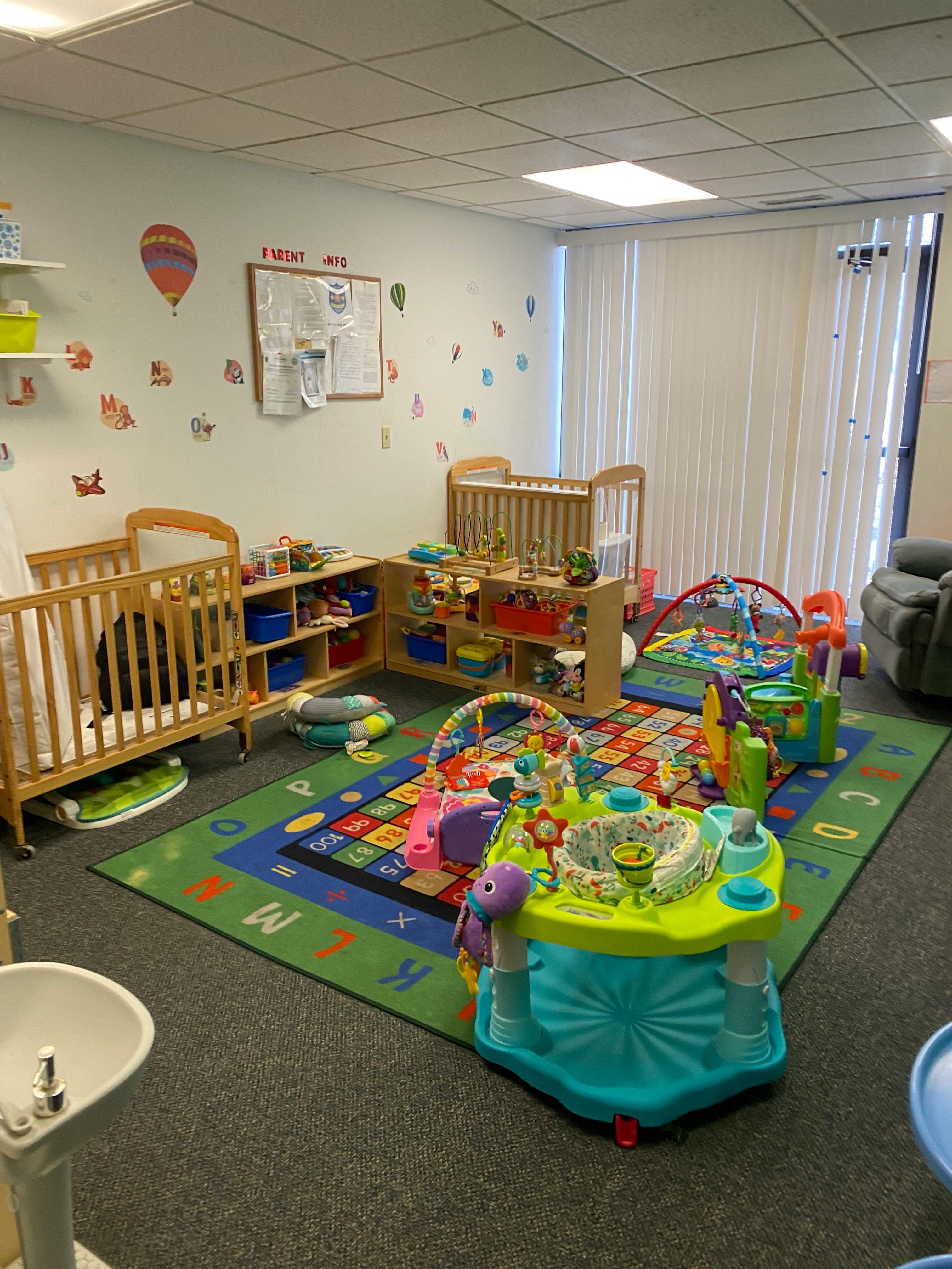 A colorful childcare room with cribs, playmats, and various infant toys