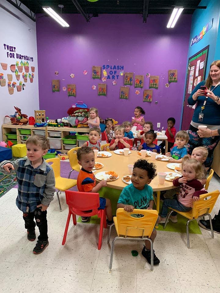 Children sitting at a round table eating, with other children standing nearby