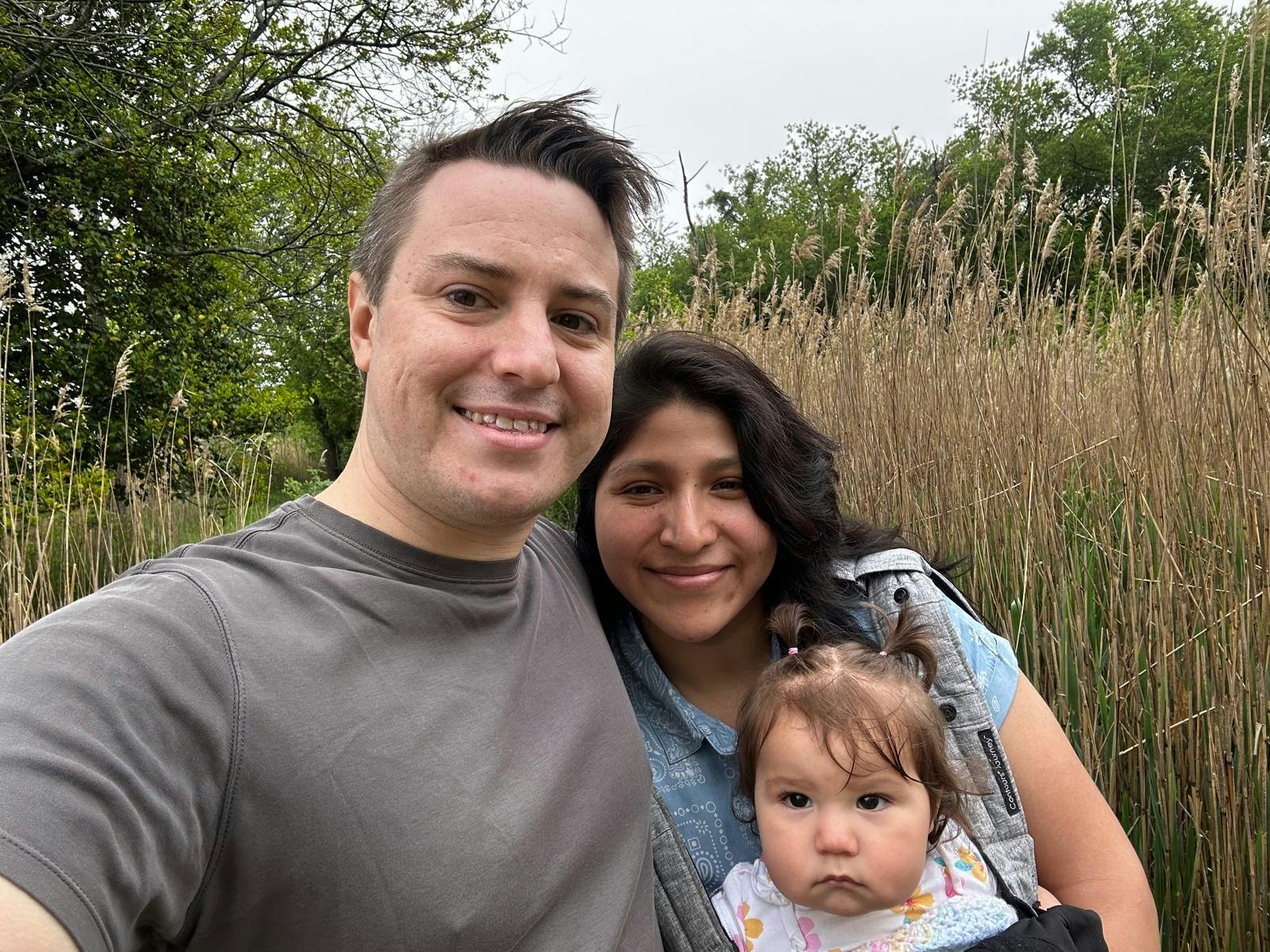 Two people standing outdoors with a child in a front carrier
