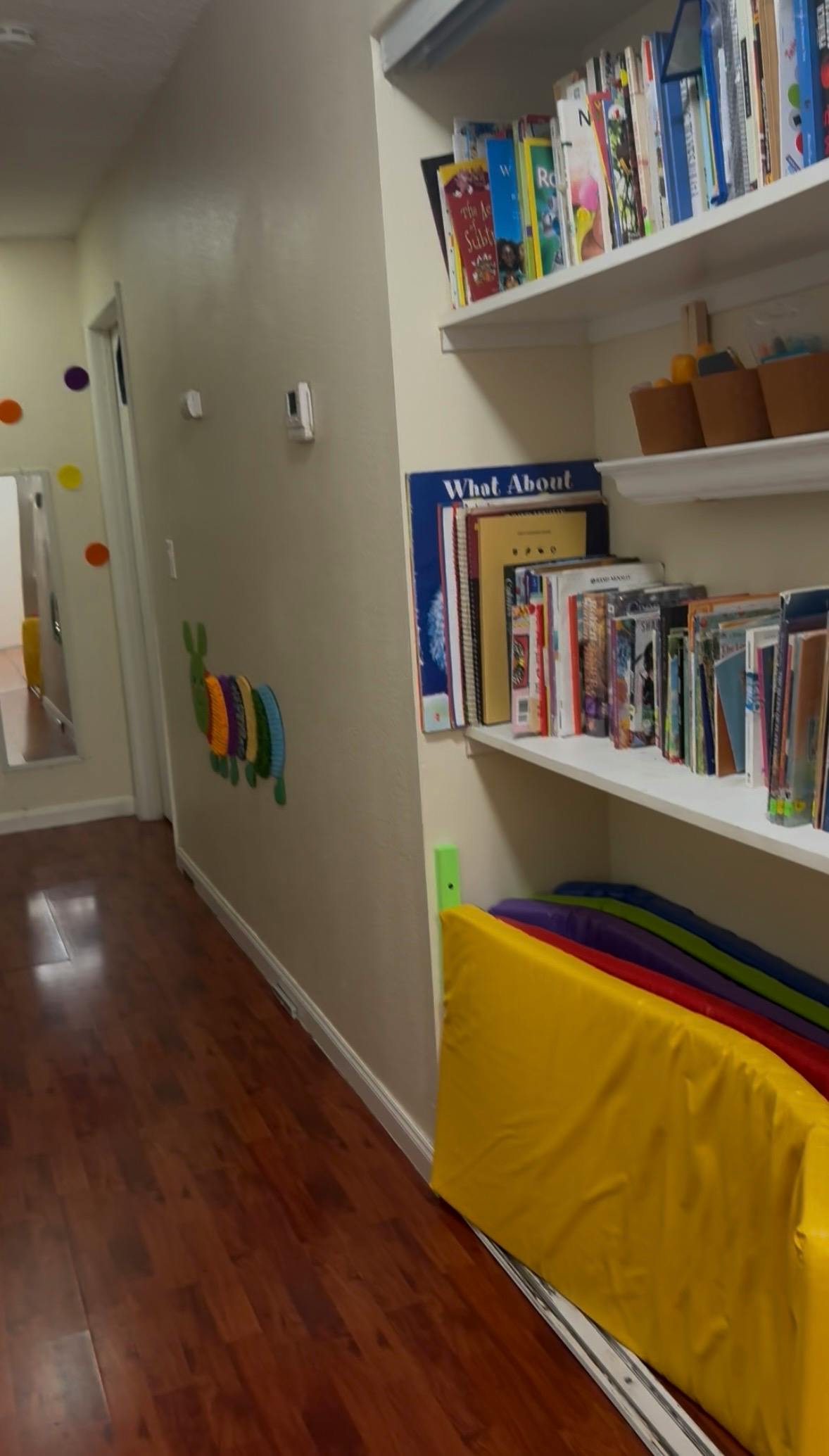 Hallway with wood floor, wall decorations, and shelves with books and colorful mats