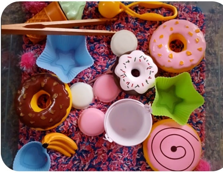 Play food donuts and toy kitchen tools on a bed of colorful rice