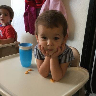 Child in a high chair with hands under chin, looking forward