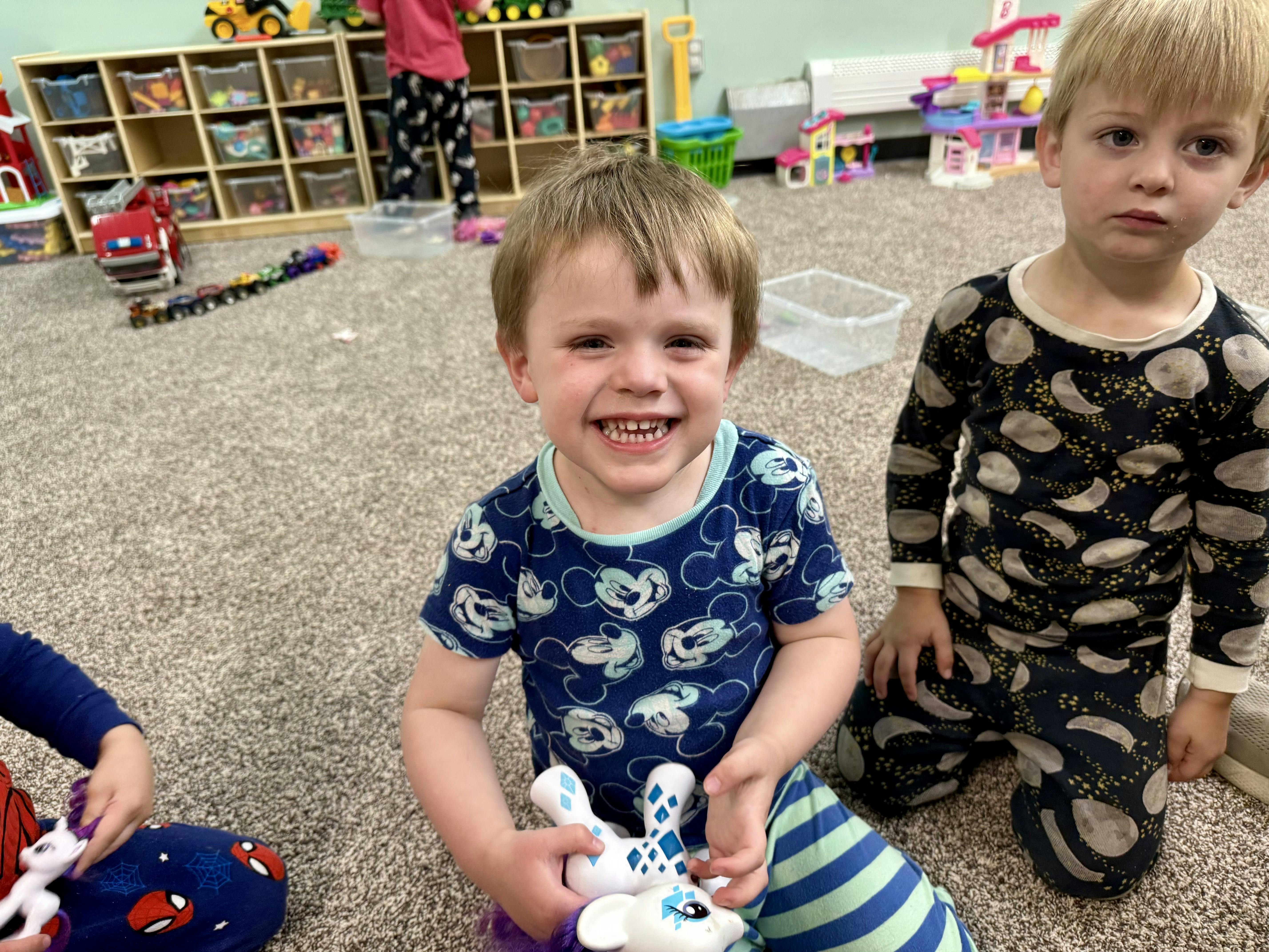 Child in blue shirt holding a toy, another child in patterned pajamas nearby