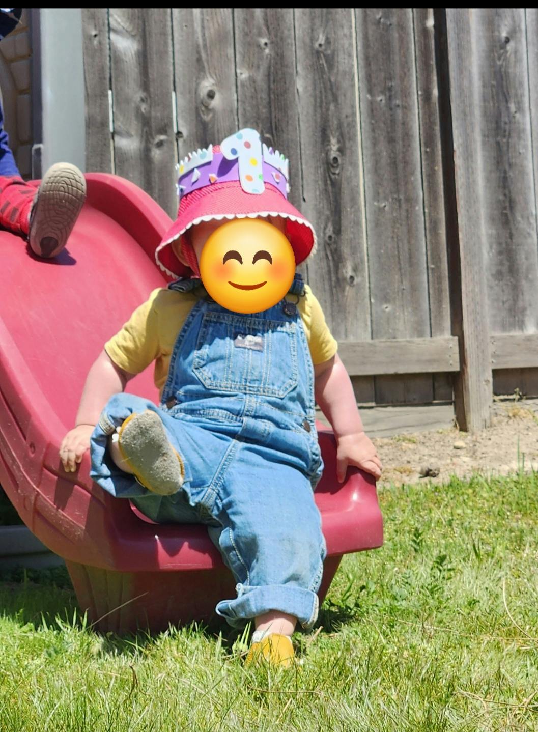 Child in overalls and a party hat sitting on a red slide