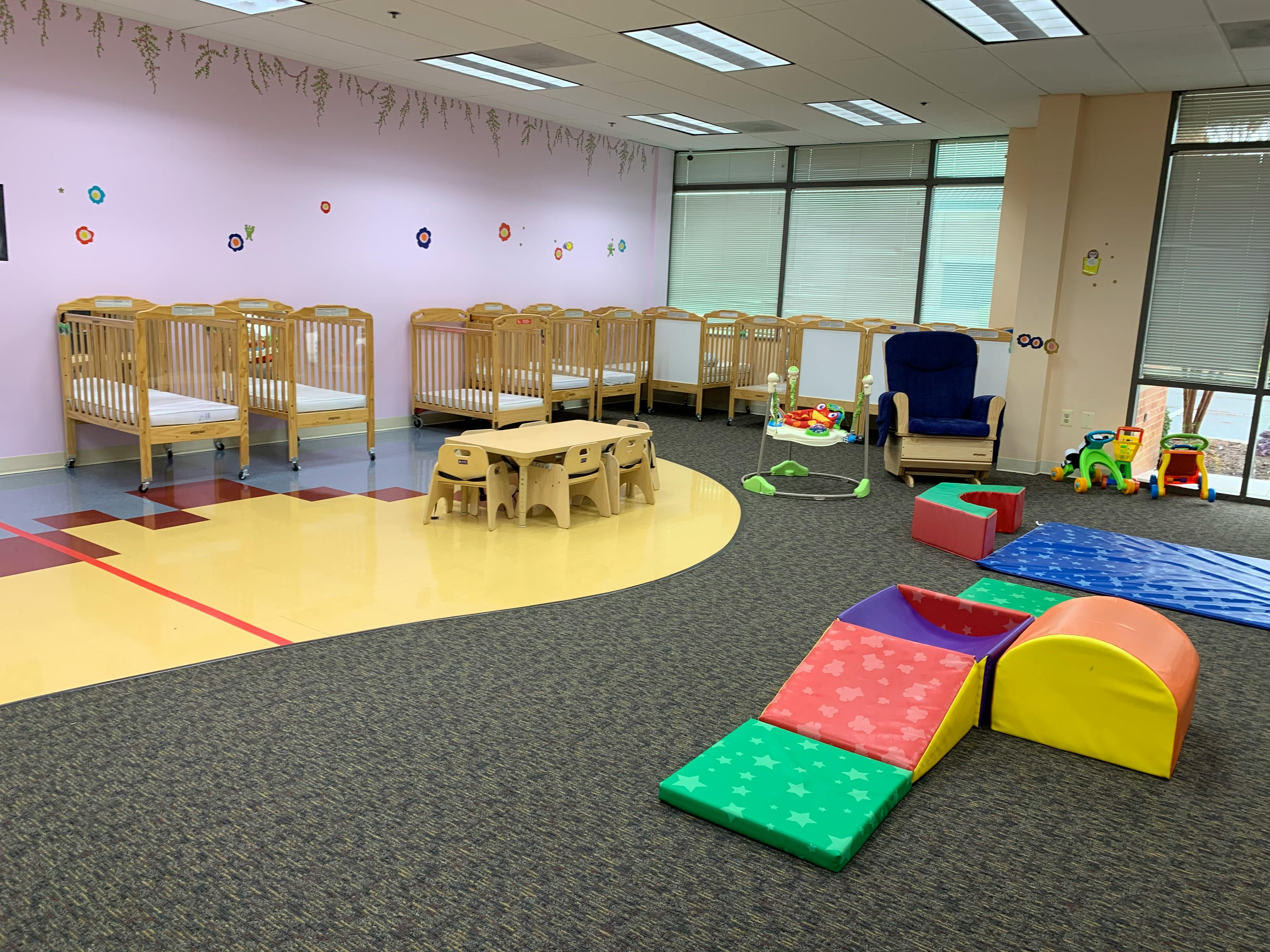 Nursery room with multiple cribs, a small table and chairs, and soft play equipment