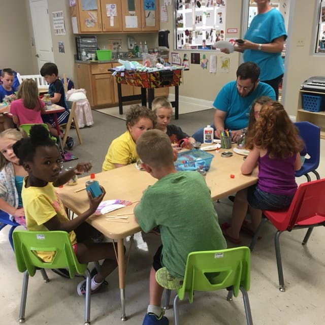 Children and adults sitting at tables in a classroom