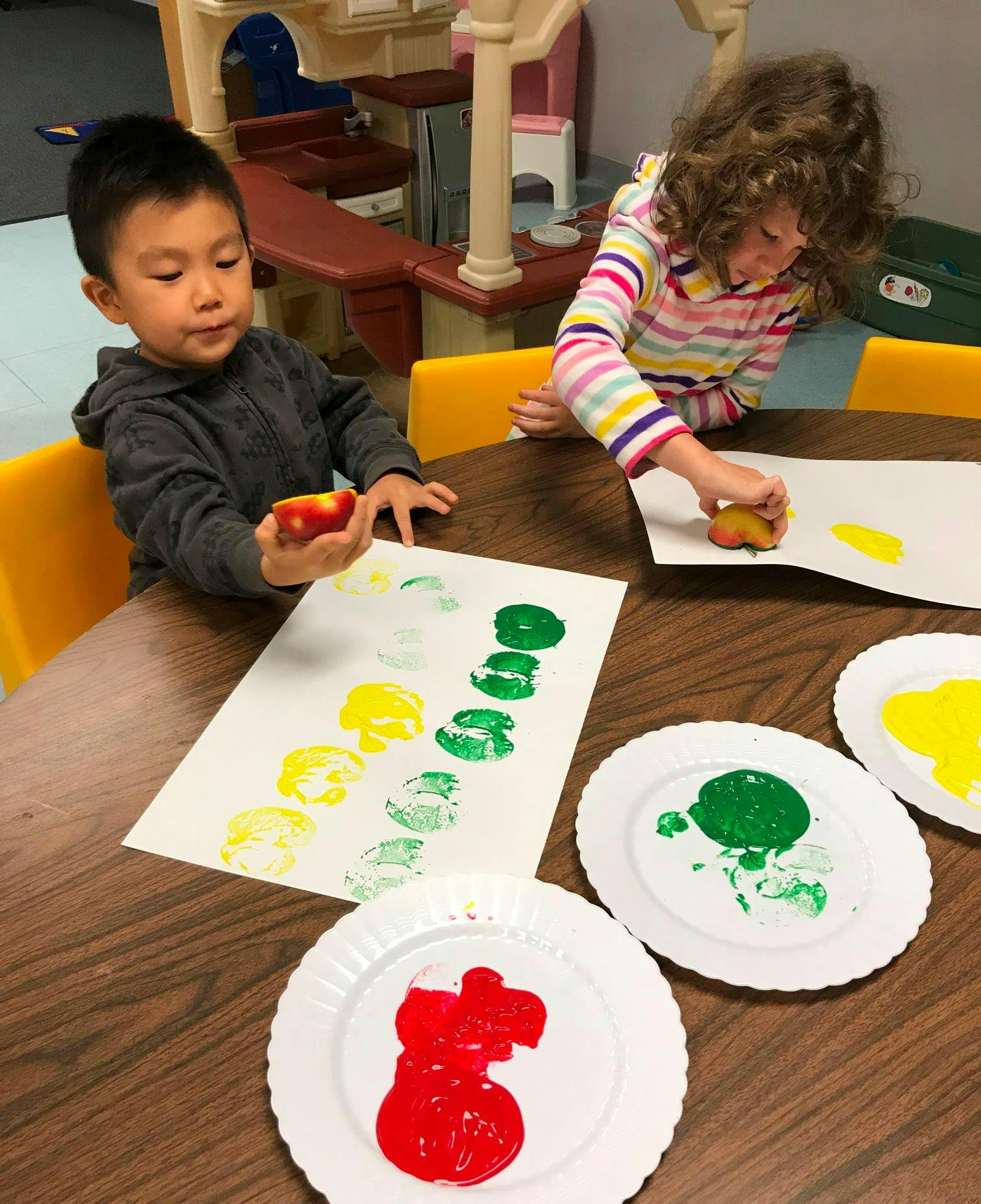 Two children doing potato stamping with red, yellow, and green paint